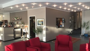 A modern lobby with red sofas, a bar area, and a staircase leading to upper floors. - Hotel Internazionale (Finale Ligure)