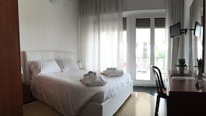 A hotel room with a large bed, a desk with a chair, and a view of the outside through a glass door. - Hotel Internazionale (Finale Ligure)