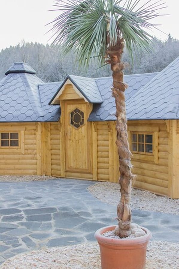 A wooden log cabin with a hexagonal door and a stone-paved driveway.