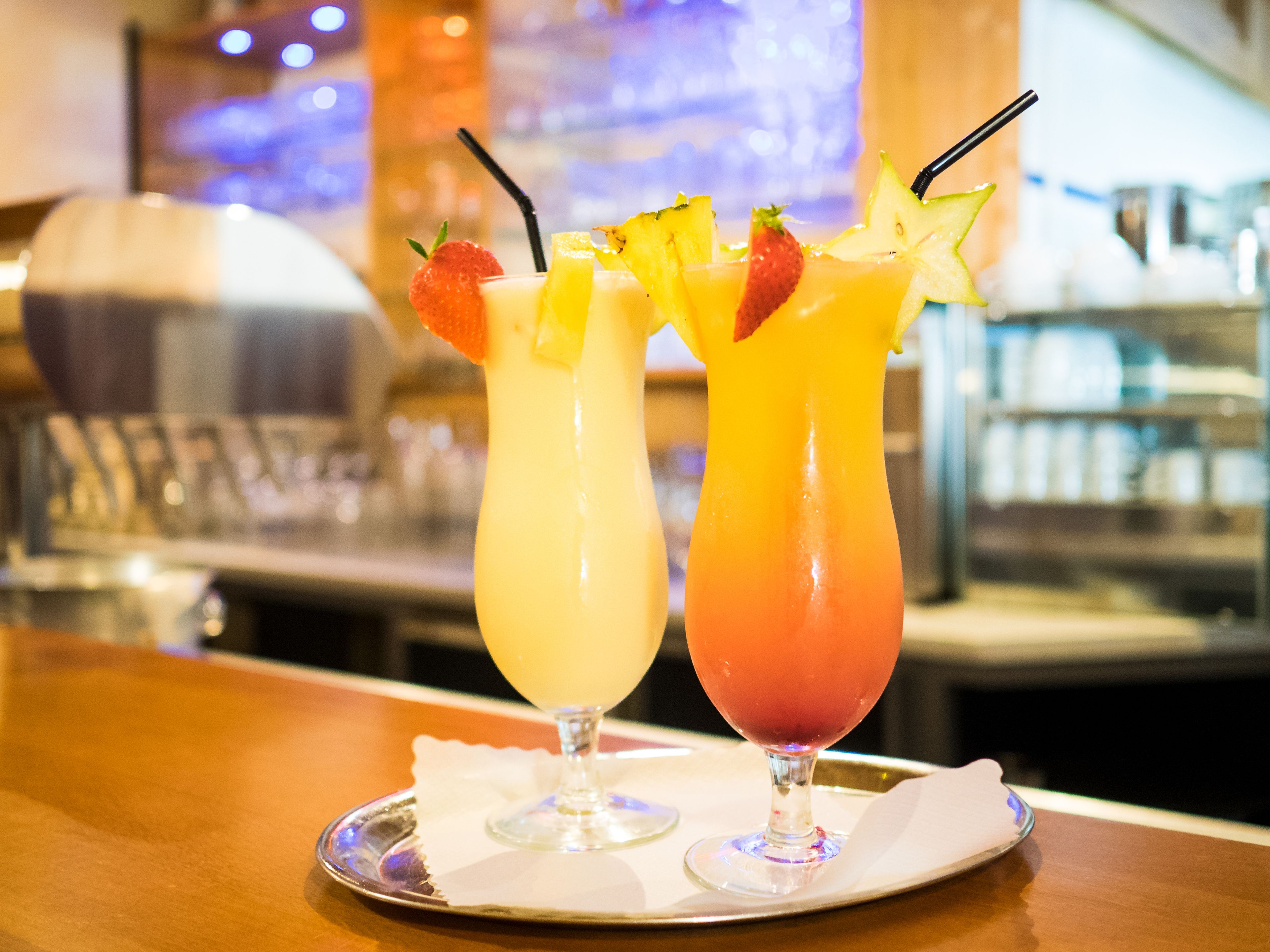 Two cocktails on a tray with a bar setting in the background.