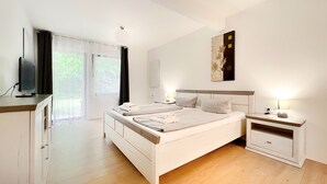 Een moderne slaapkamer met een groot bed, nachtkastjes, een flatscreen televisie en een groot raam met gordijnen.