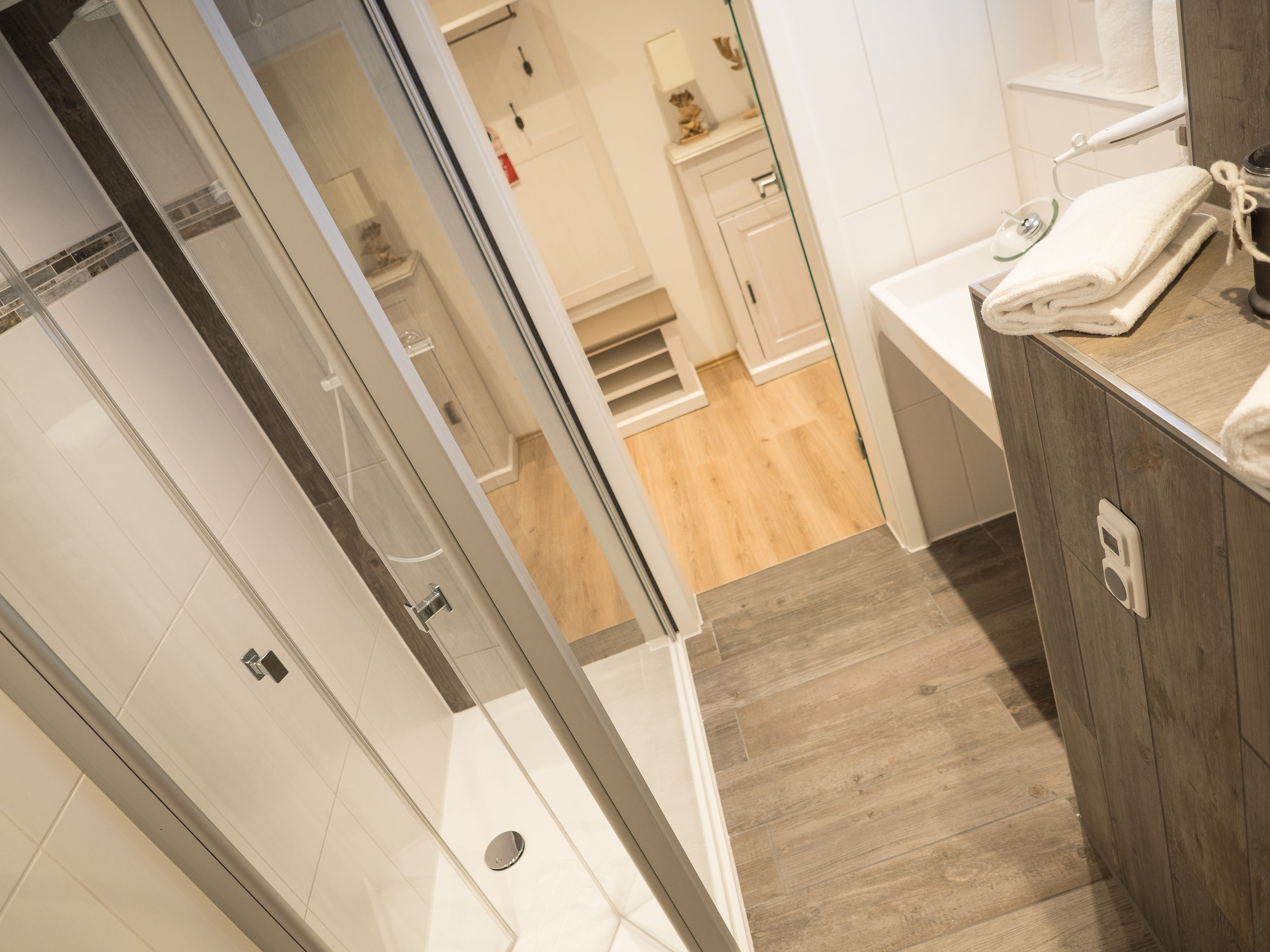 A modern bathroom with a glass shower door, wooden flooring, and a white sink with a towel on the counter.