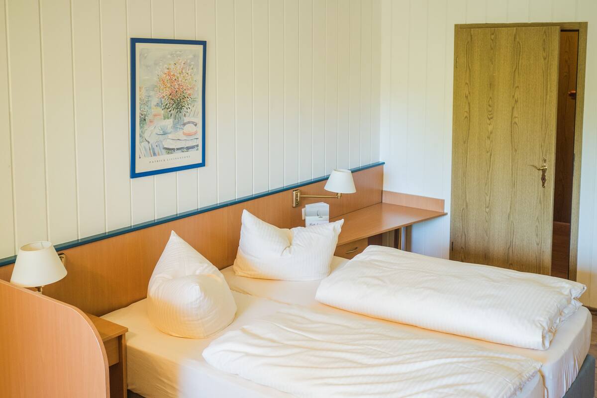 Een hotelkamer met een bed, nachtkastjes, een lamp, een lijst met een foto aan de muur en een houten deur.