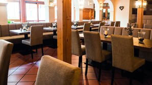 Een restaurant met houten balken, gebogen ramen en ruimtes met zitjes. Tafels zijn gedekt met kaarsen en glazen.