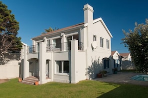 A two-story house with a balcony, a swimming pool, and a well-maintained lawn.