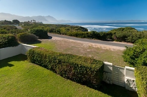 A coastal property with a paved driveway leading to a grassy area, surrounded by dense greenery and a view of the ocean.
