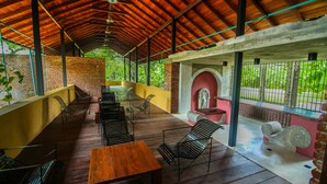 An outdoor covered patio with wooden flooring, metal chairs, and a wooden table.