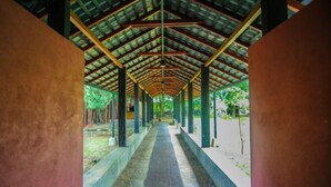 A covered walkway with a tiled floor and metal beams, surrounded by greenery.