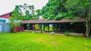 A covered outdoor area with a thatched roof, surrounded by lush greenery and a grassy lawn.