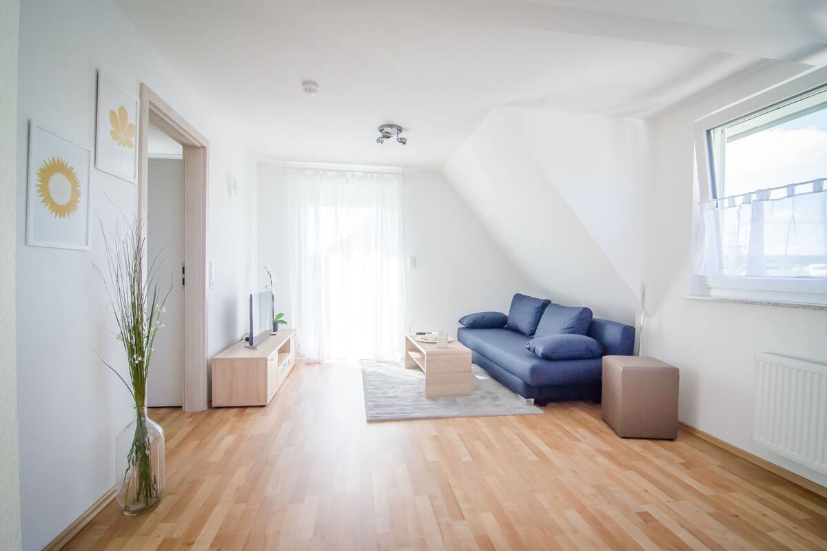 Una sala moderna con un sofá azul, una mesa de centro de madera y un jarrón de cristal con plantas.