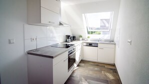 A compact kitchen with white cabinets, a stainless steel countertop, a built-in oven, and a window providing natural light. - BB-Apartment (Boeblingen)