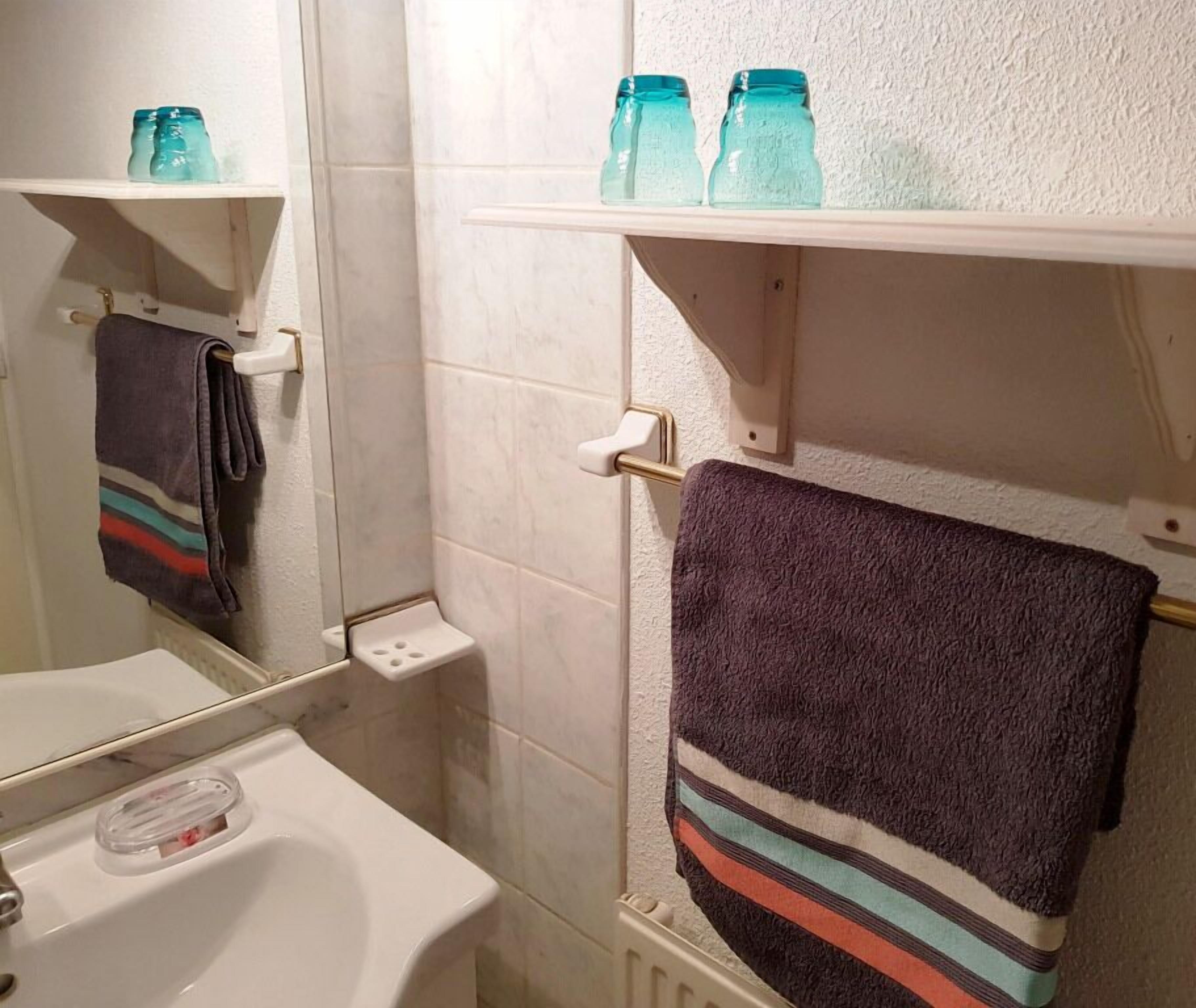 Een badkamer met een witte wastafel, een spiegel, een handdoekhouder met een gestreepte handdoek, en planken met blauwe glazen potten.