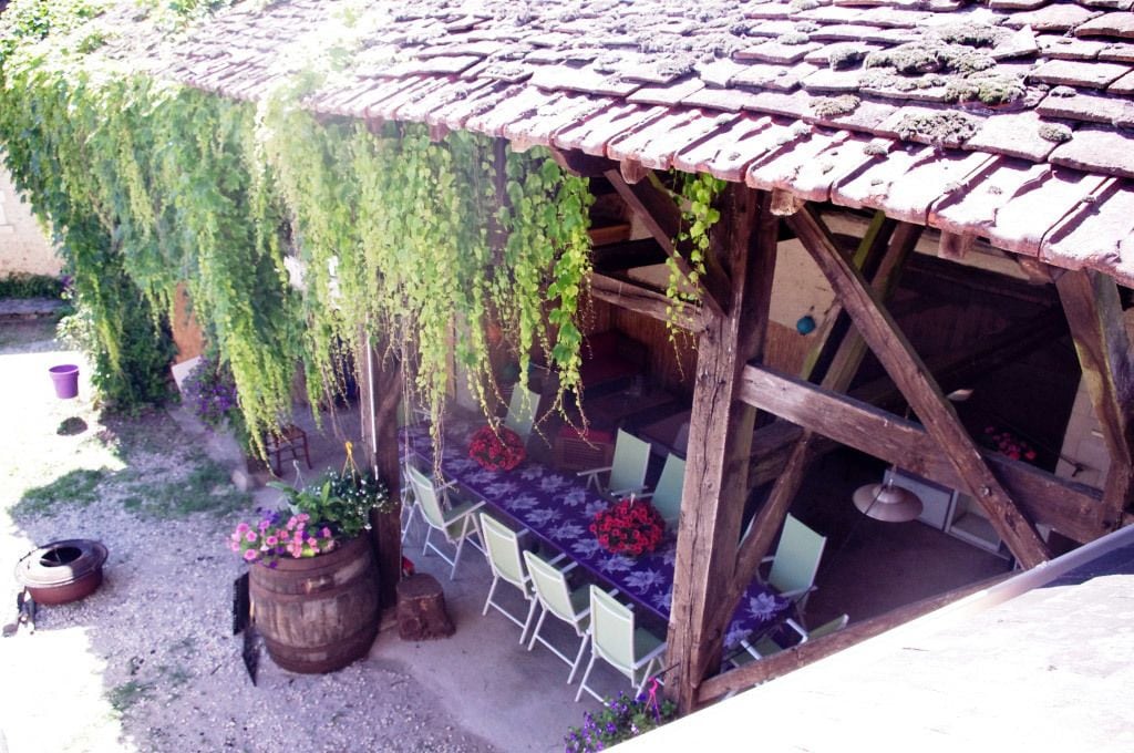 Ein rustikaler Sitzbereich im Freien mit einer Holz-Pergola, einem gedeckten Tisch und Blumentöpfen.