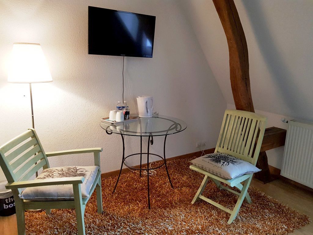 Une pièce avec un téléviseur fixé au mur, une table ronde en verre, deux chaises, une lampe et un radiateur.