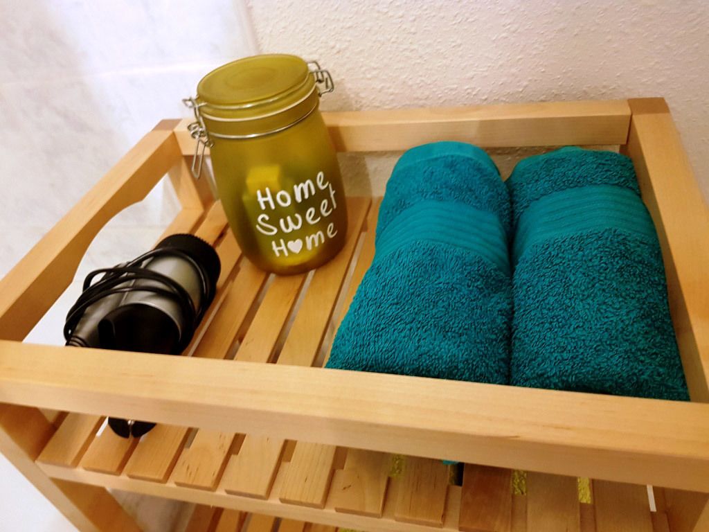 A wooden tray with a green jar labeled "Home Sweet Home," a camera, and two teal towels.