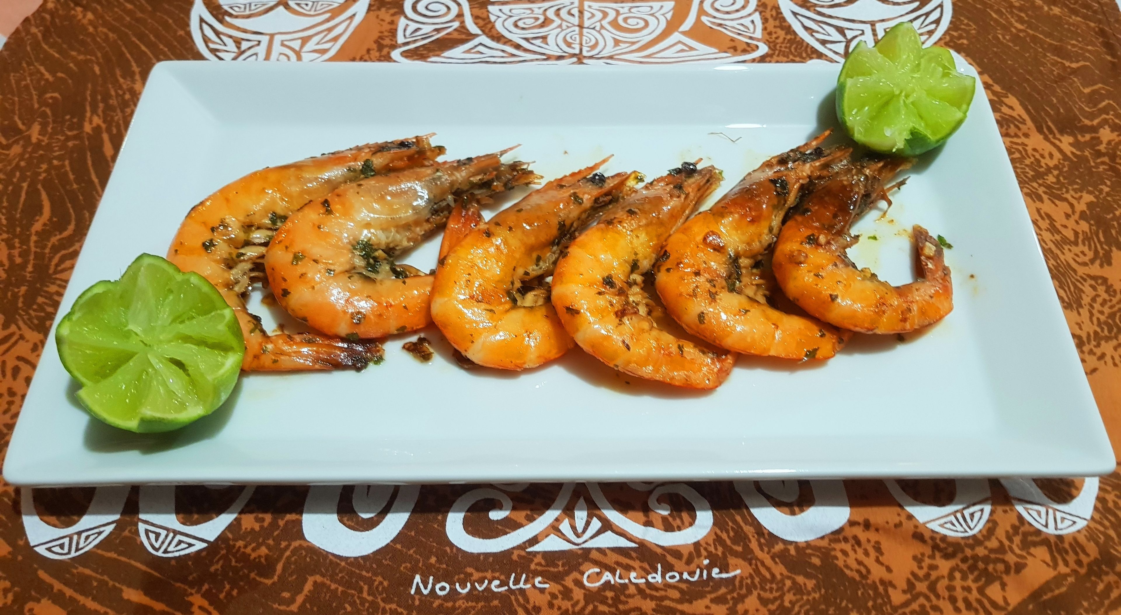 A plate of cooked shrimp with lime wedges on a white rectangular plate.