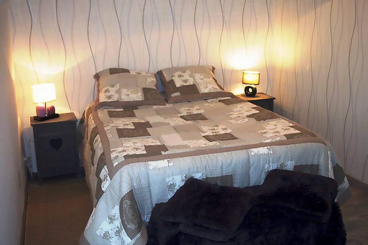 A bed with a quilt, two bedside tables with lamps, and a patterned wall.