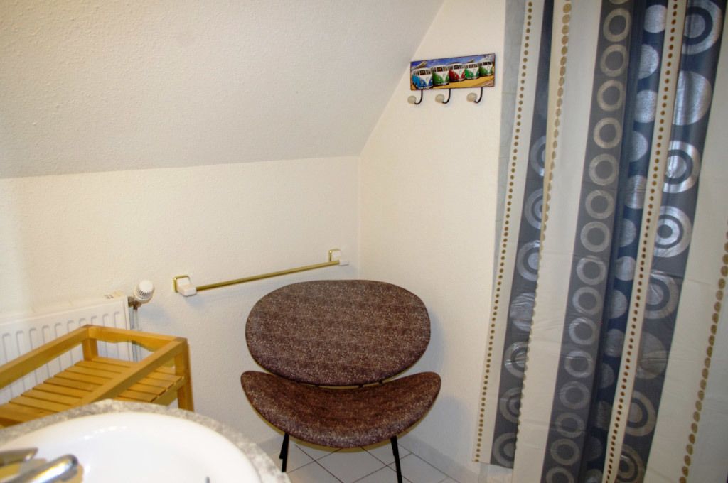 A bathroom with a wooden chair, a towel rack, a radiator, and patterned curtains.