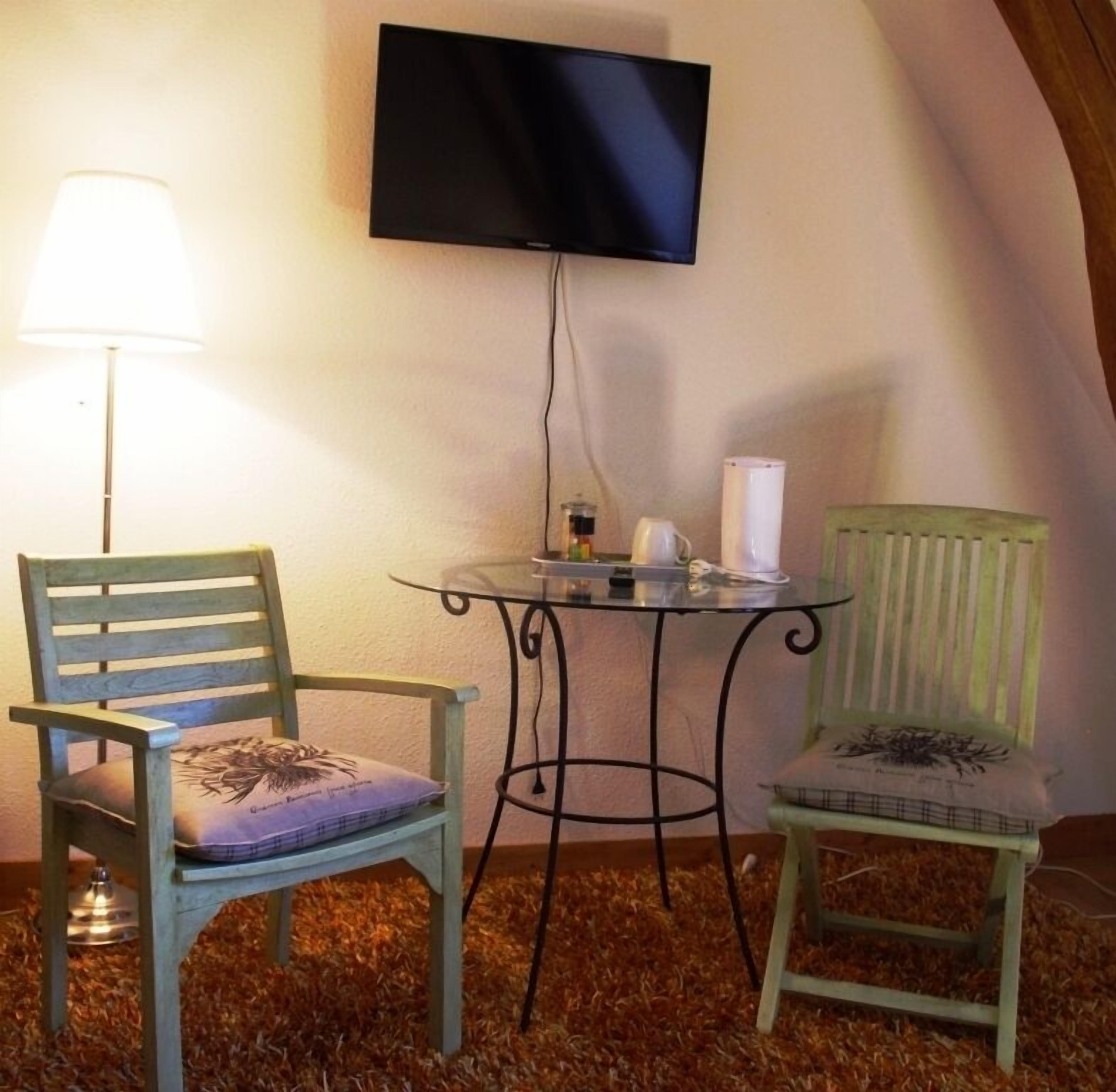 Une pièce confortable avec un téléviseur fixé au mur, une petite table ronde avec une lampe et deux chaises.
