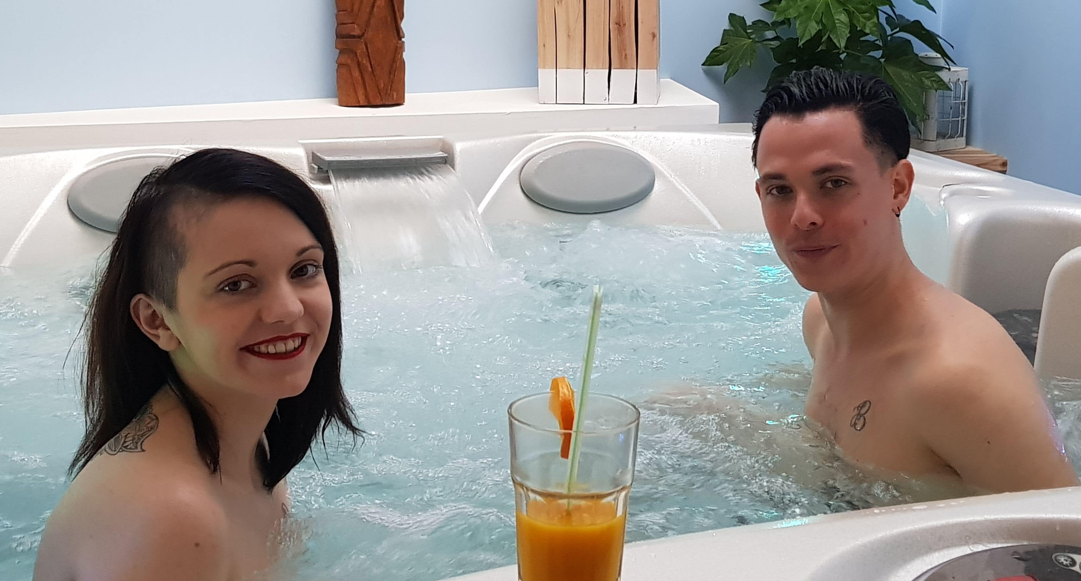 A couple in a hot tub with a glass of orange juice.