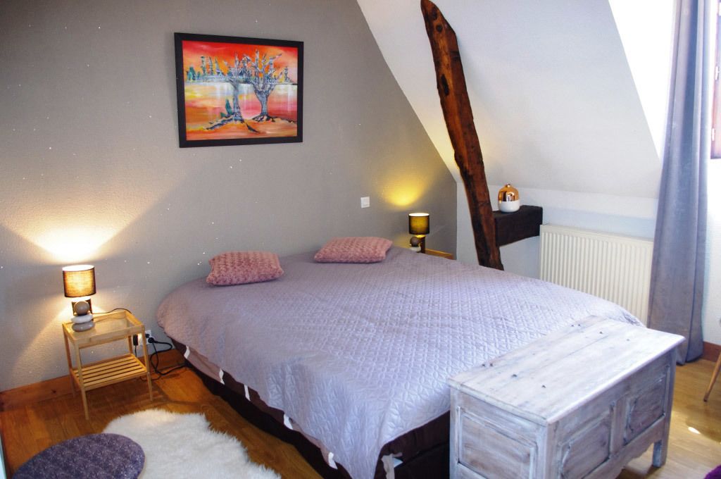 A bedroom with a bed, a nightstand, a lamp, a painting, and a wooden beam.