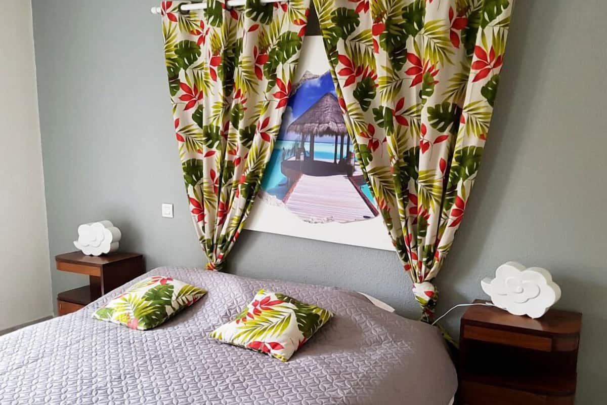 A bedroom with a bed, two nightstands, and a tropical-themed curtain.
