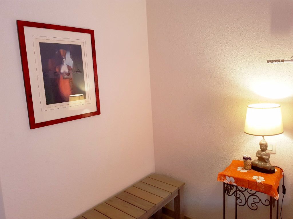Een kamer met een lijstafbeelding aan de muur, een bank en een tafel met een lamp en decoratieve objecten.