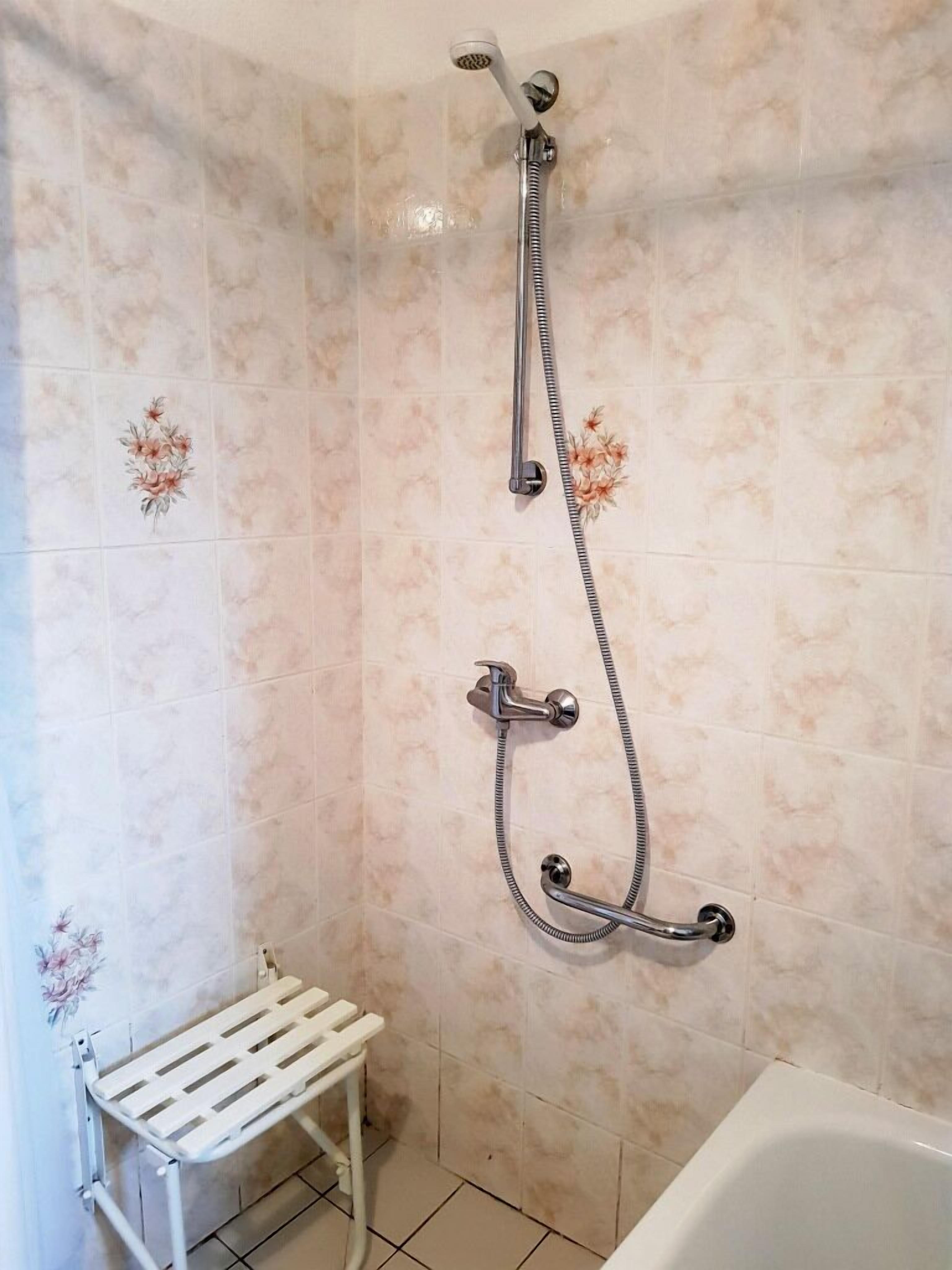 A bathroom with a shower, a white bathtub, and a white shelf unit.