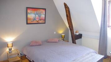Un dormitorio con cama, dos lámparas de noche, una mesita de noche, un cabecero de madera, un cuadro en la pared y una ventana con cortinas.