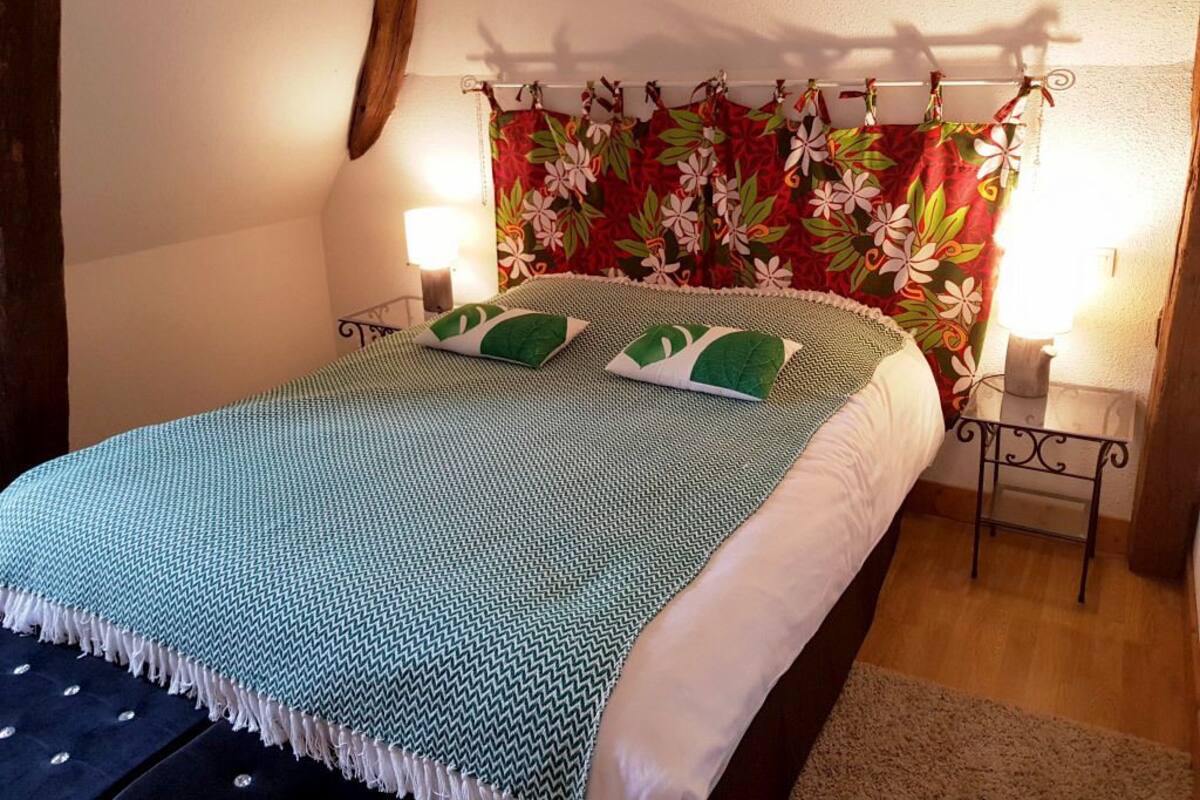 A neatly made bed with a patterned bedspread and pillows, a floral curtain, and bedside lamps.