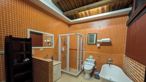 Un baño con paredes de azulejos anaranjados, una ducha, un inodoro, un lavabo y una bañera.
