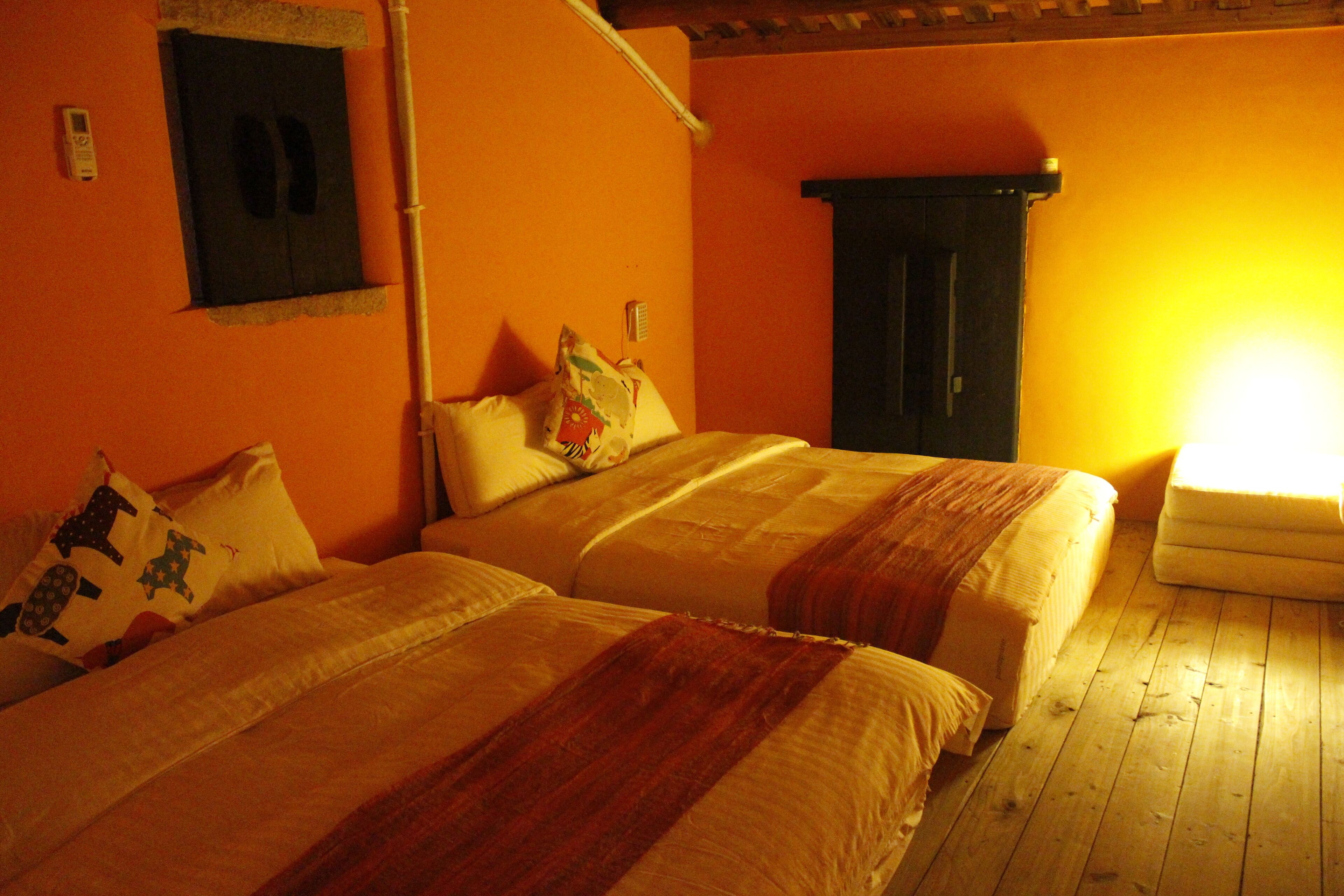 A room with two beds, a wooden floor, and a wall-mounted heater.