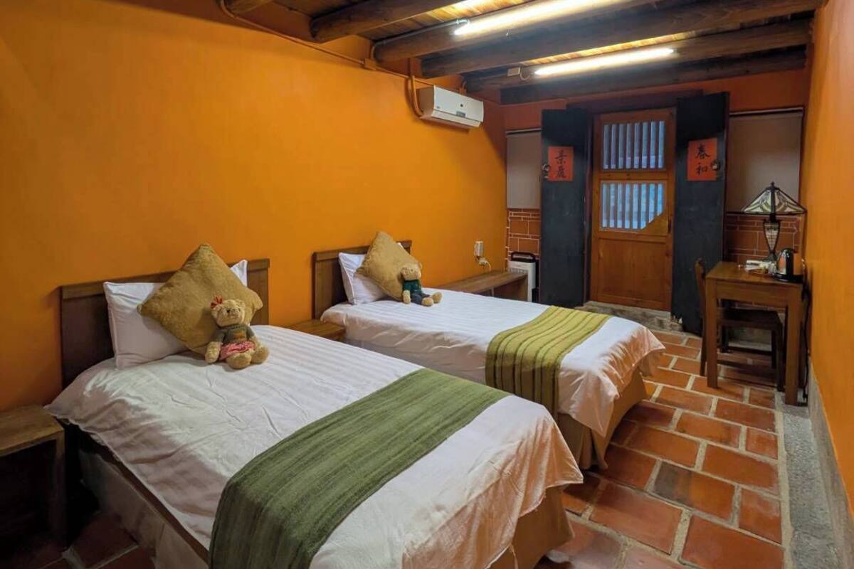 Une chambre avec deux lits, un plafond en bois, des murs orange et un sol carrelé.