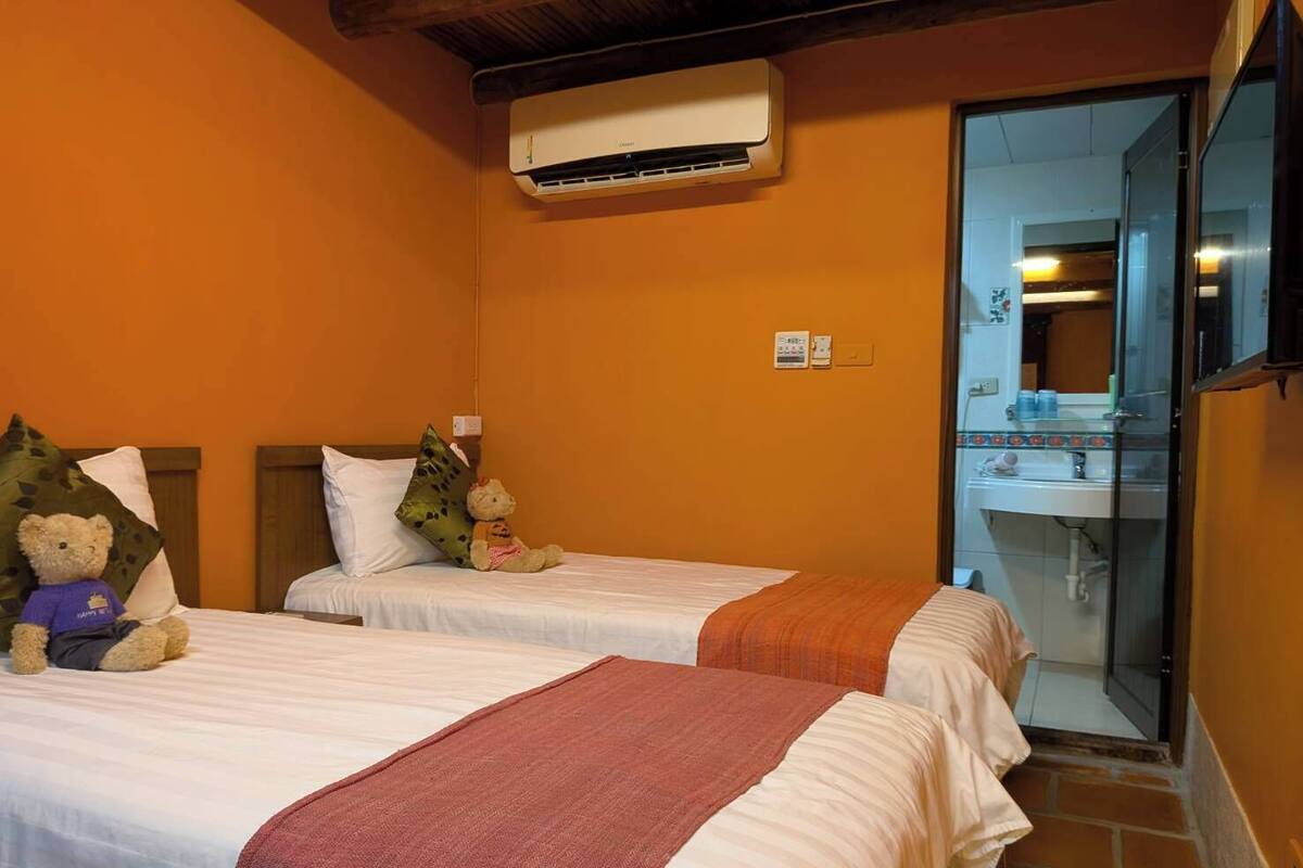 Une chambre d’hôtel avec deux lits, une salle de bain avec une douche en verre et un climatiseur fixé au mur.