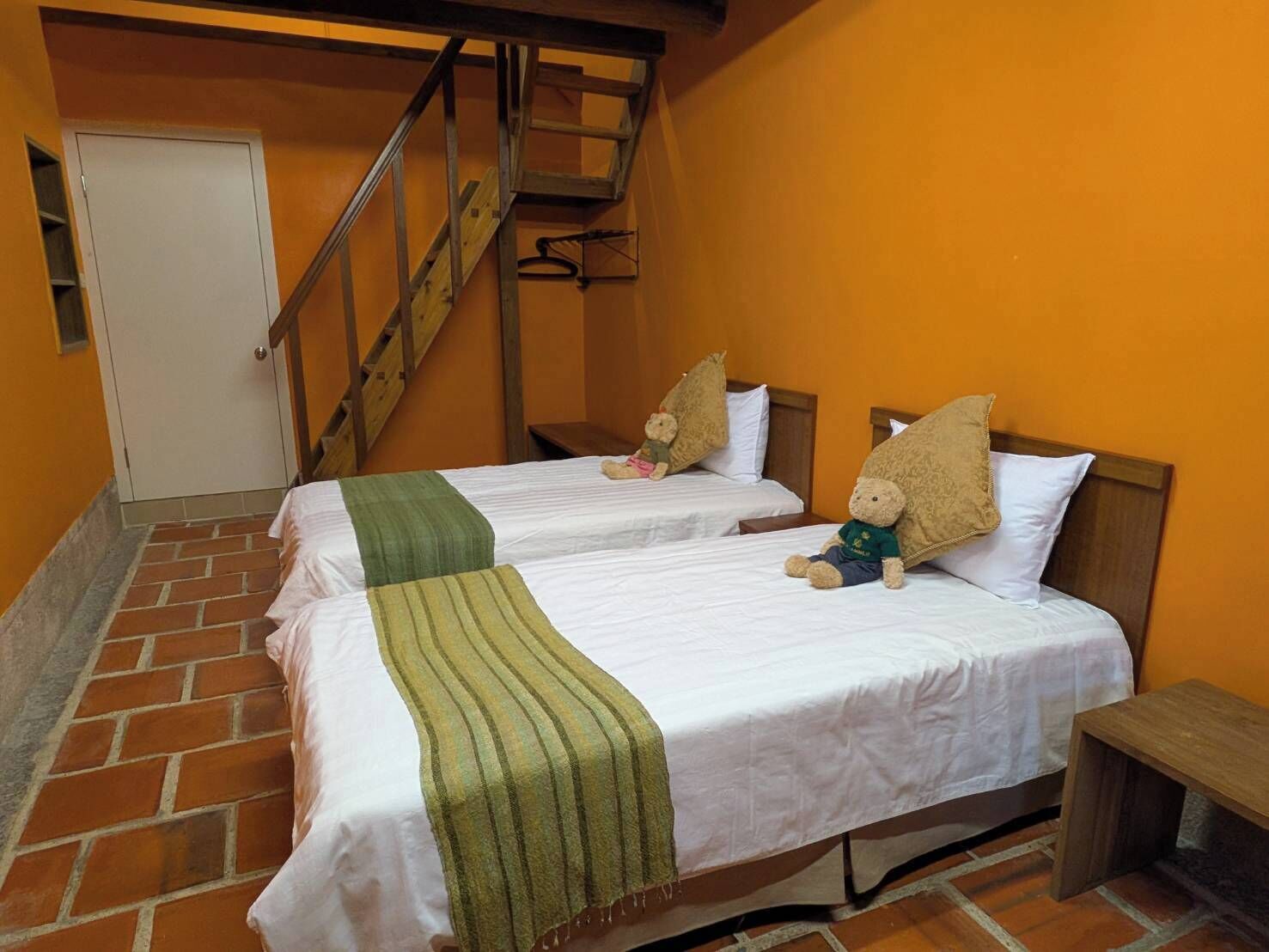A room with two beds, a wooden staircase, and a door.