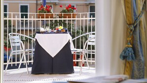 Ein Balkon mit Tisch für Zwei, umgeben von weißen Stühlen und Kübelpflanzen mit roten Blüten.