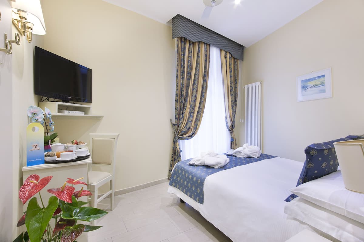 A hotel room with a bed, a television, a desk with a chair, and a window with curtains.