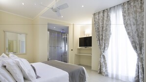 Ein modernes Hotelzimmer mit einem großen Bett, einem Deckenventilator, einem Fernseher und einem Duschbereich.