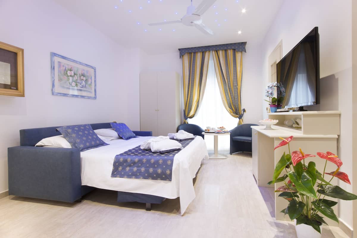 A modern hotel room with a bed, a TV, a desk, and a potted plant.