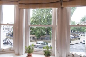 A view from a window with curtains, overlooking a street with parked cars and a roundabout.