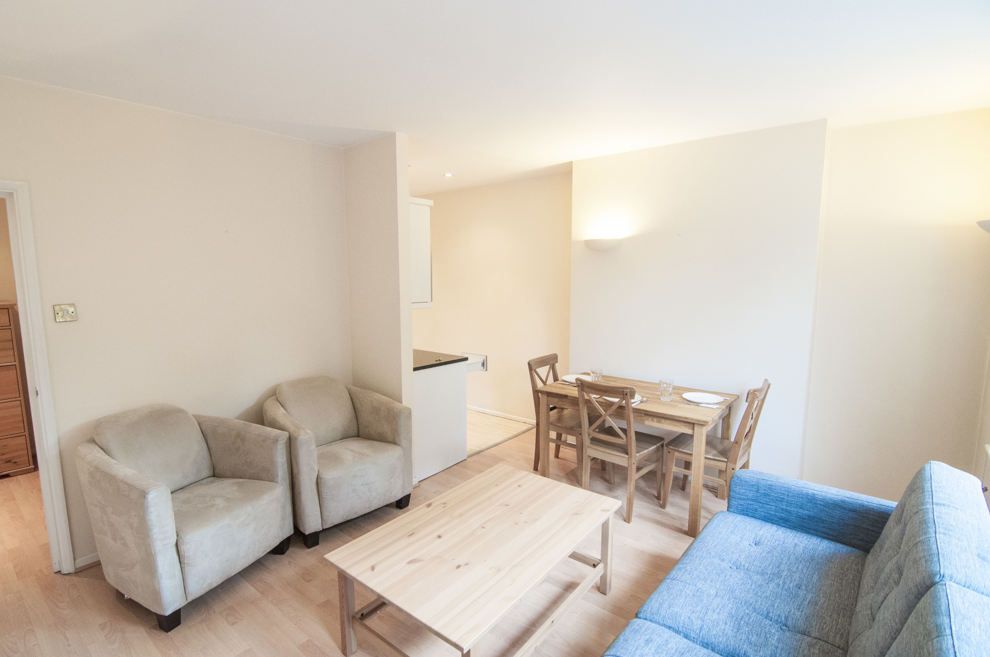 A living room with a blue sofa, two beige armchairs, a wooden coffee table, and a dining table with chairs.