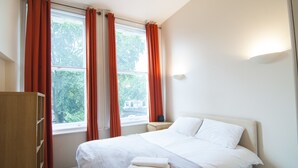 A bedroom with a bed, a nightstand, a wardrobe, and a window with curtains. - CityGate Farringdon (London)