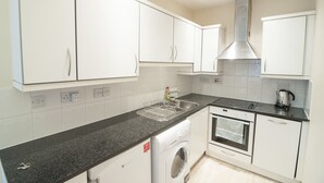 A modern kitchen with white cabinets, a stainless steel range hood, a built-in oven, and a washing machine. - CityGate Farringdon (London)