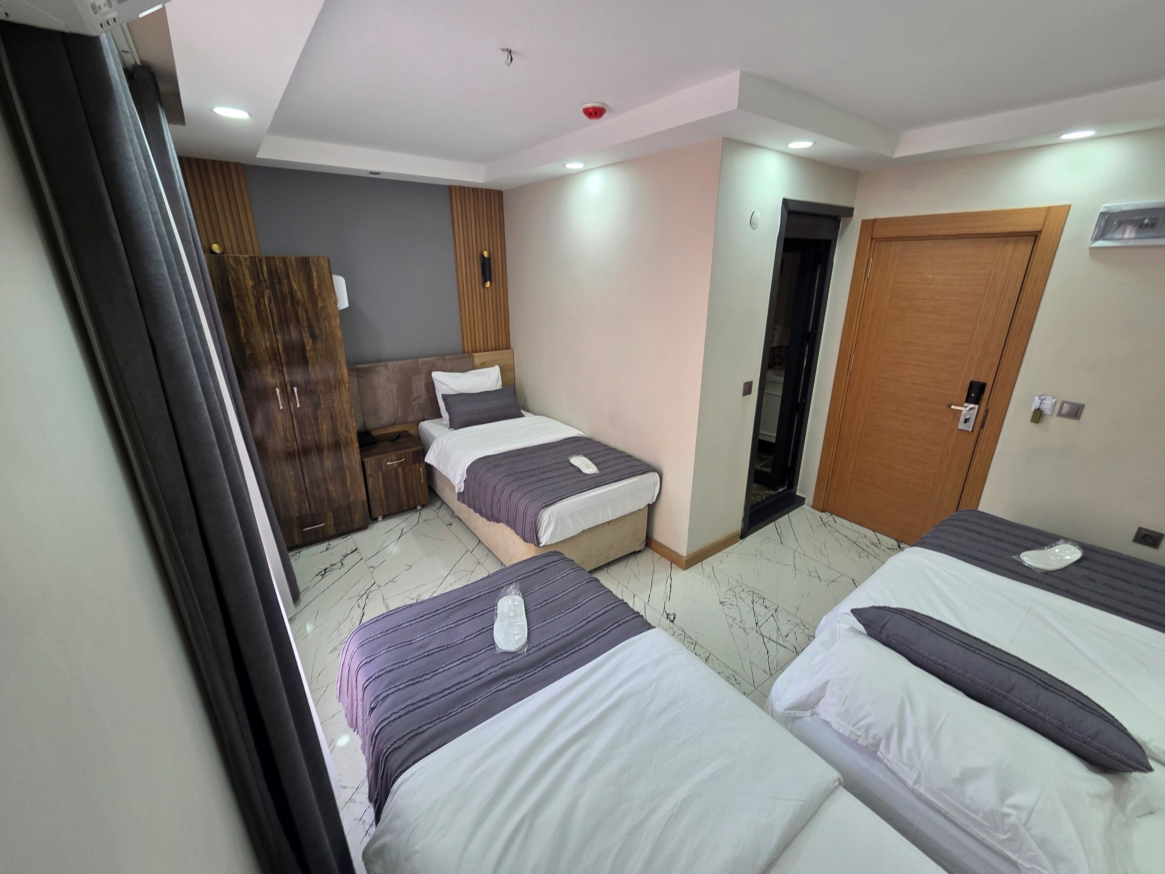 A hotel room with two beds, a wardrobe, a desk, and a door leading to another room.