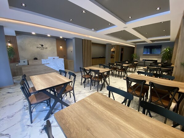 A modern restaurant with marble flooring, wooden tables and chairs, and recessed ceiling lighting.
