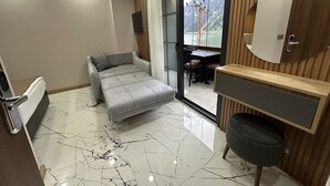 Una habitación de hotel moderna con sofá cama, una mesita, una silla, un espejo y vistas a un paisaje montañoso a través de una puerta corredera de vidrio.