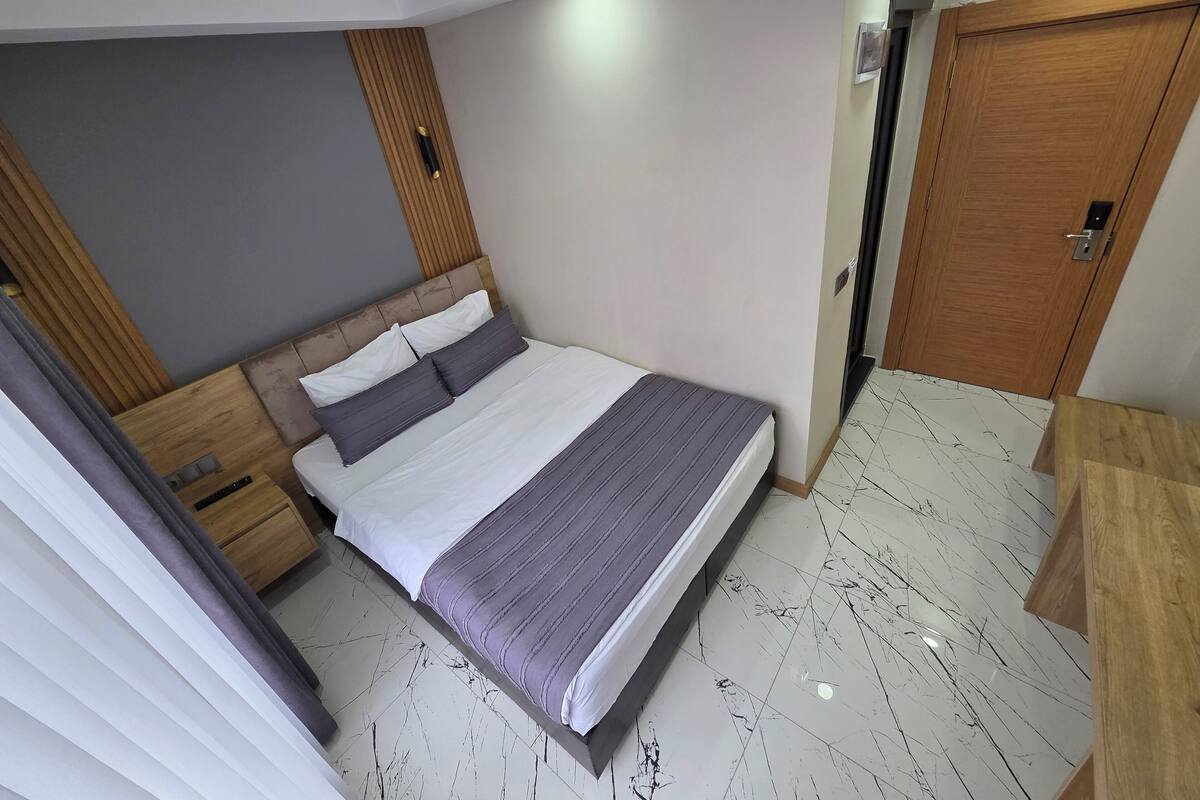 Een moderne hotelkamer met een groot bed, een houten hoofdbord, een garderobe en een badkamers deur.