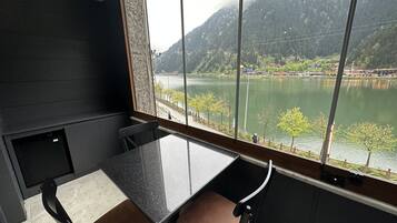 Una habitación con un amplio ventanal con vista a un lago y montañas. Adentro hay una mesa y sillas.