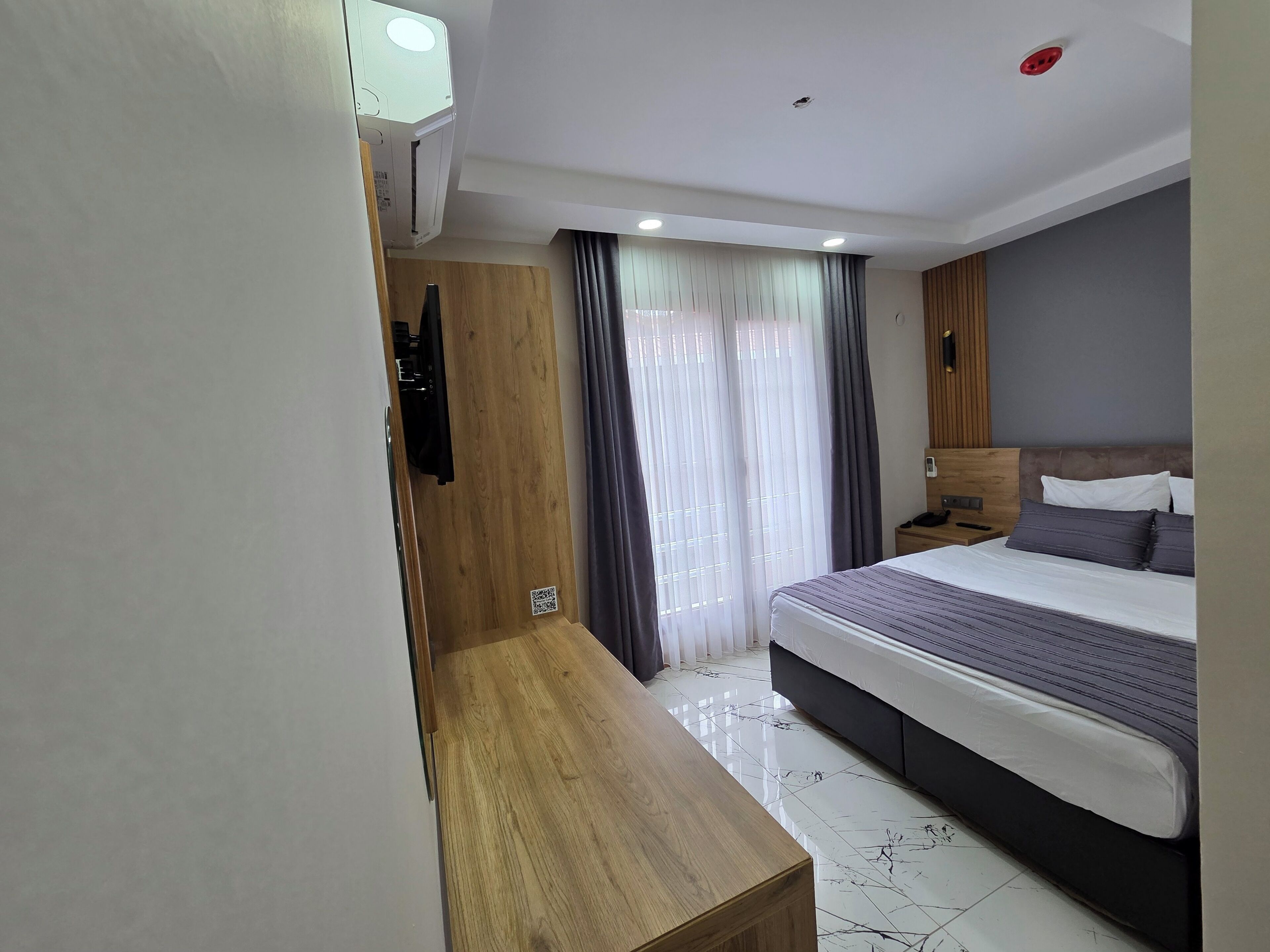 Habitació d'hotel moderna amb llit, taula de nit i televisió integrada.