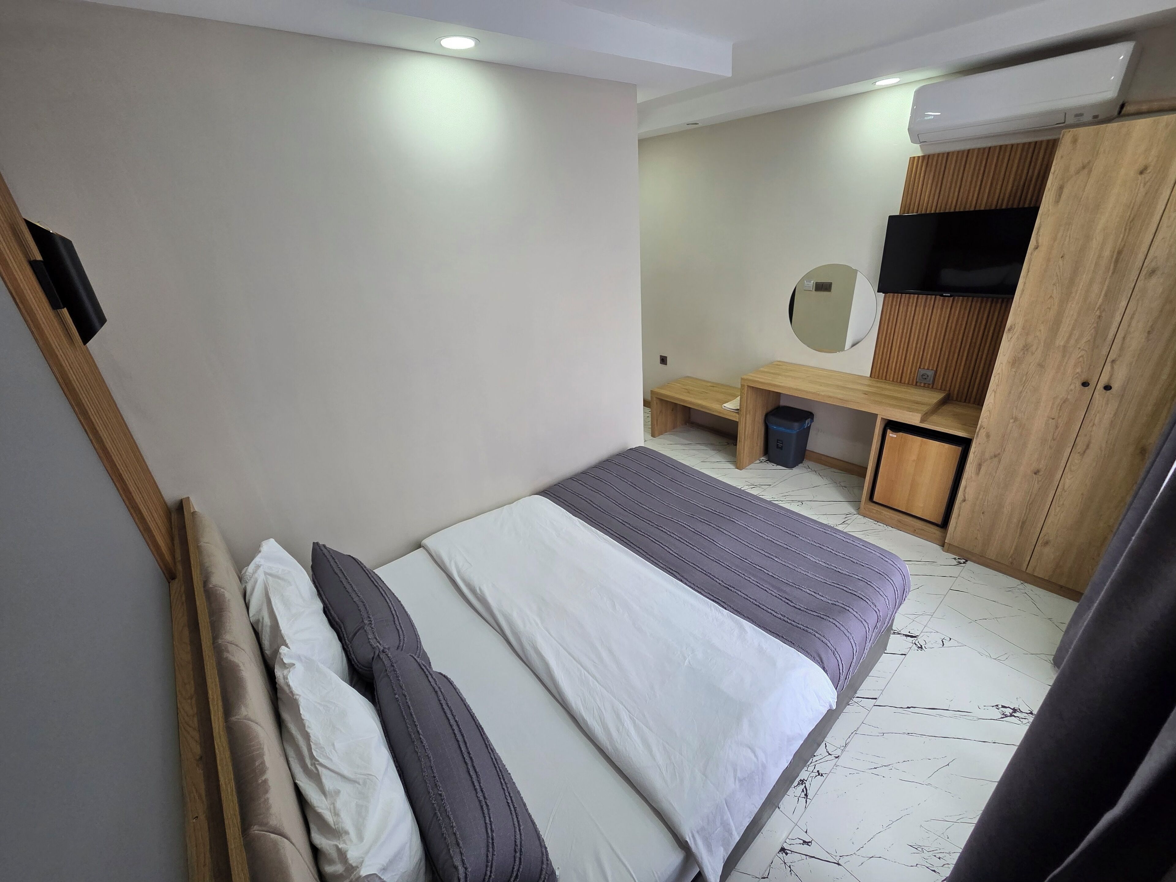 A bedroom with a bed, a bench, a small table, a mirror, and a wardrobe.